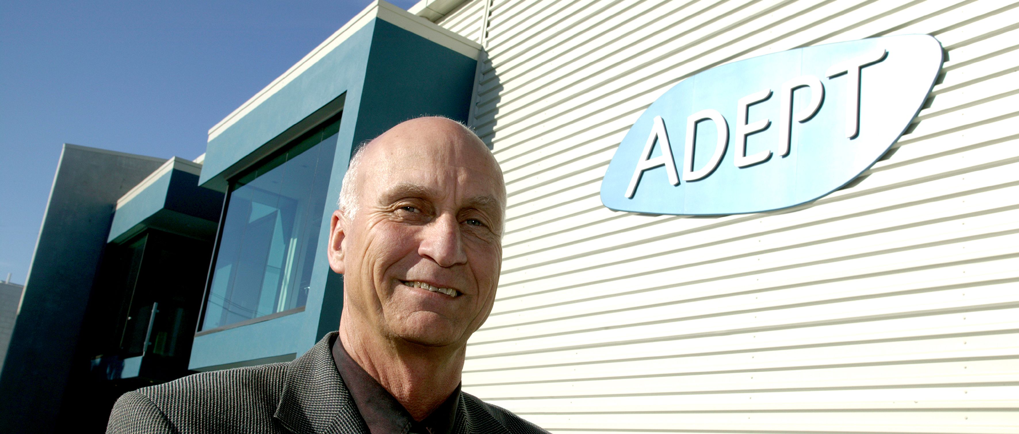 Bald man smiling in front of a building with an ADEPT sign.
