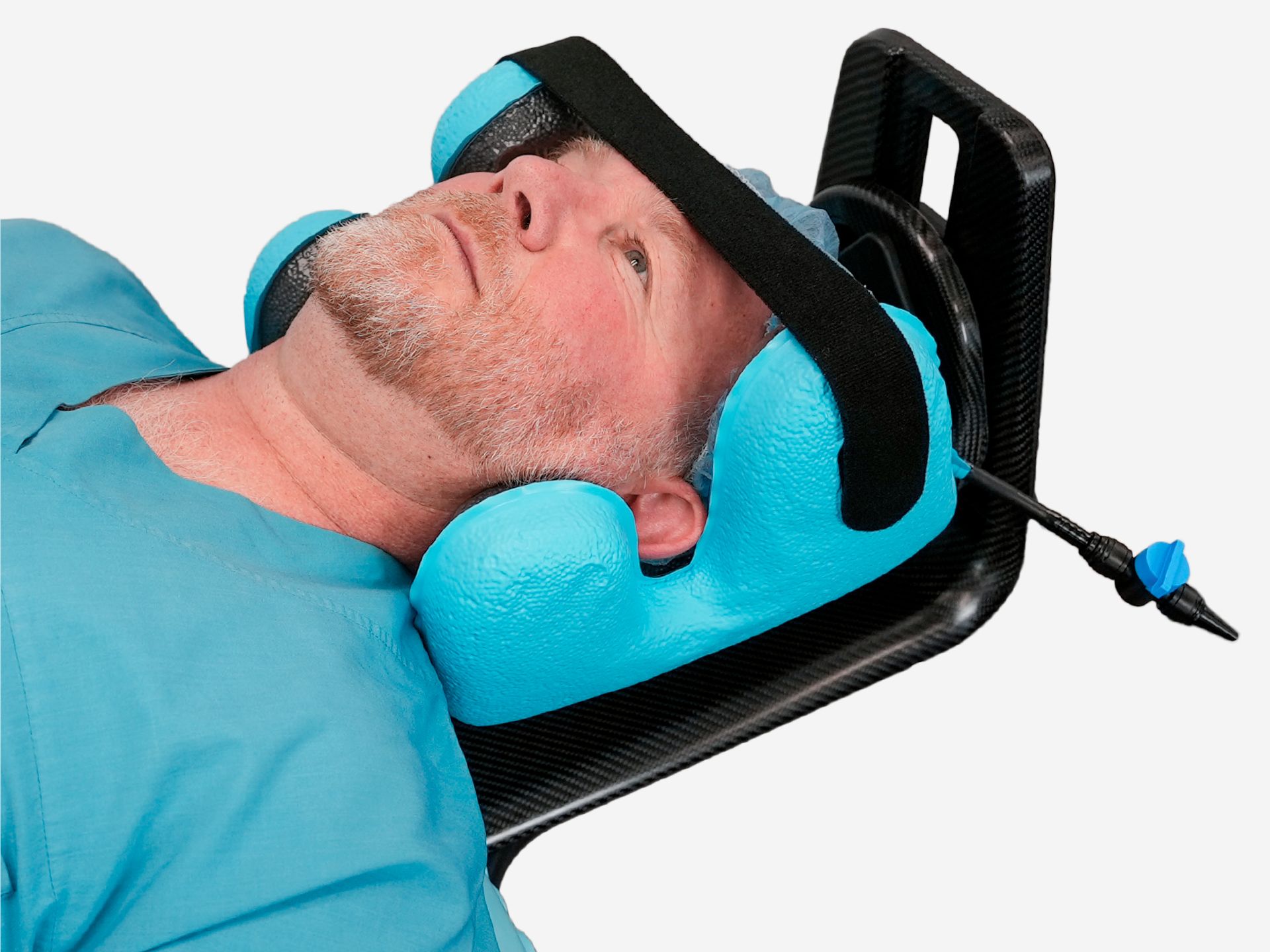 Man in medical scrubs and cap with his head secured in a blue contoured medical head support device.