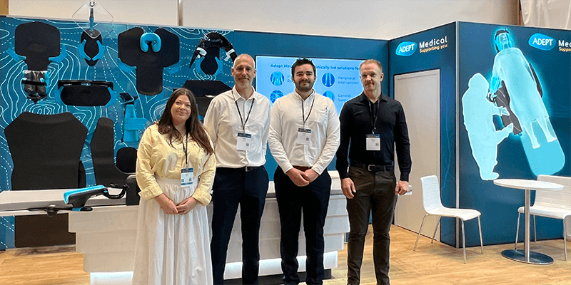 A woman and three men stand in front of the ADEPT Medical exhibition booth displaying medical support devices.