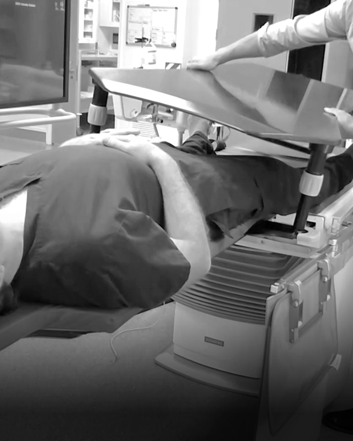 Medical professional adjusts equipment over a patient's legs on a medical table.