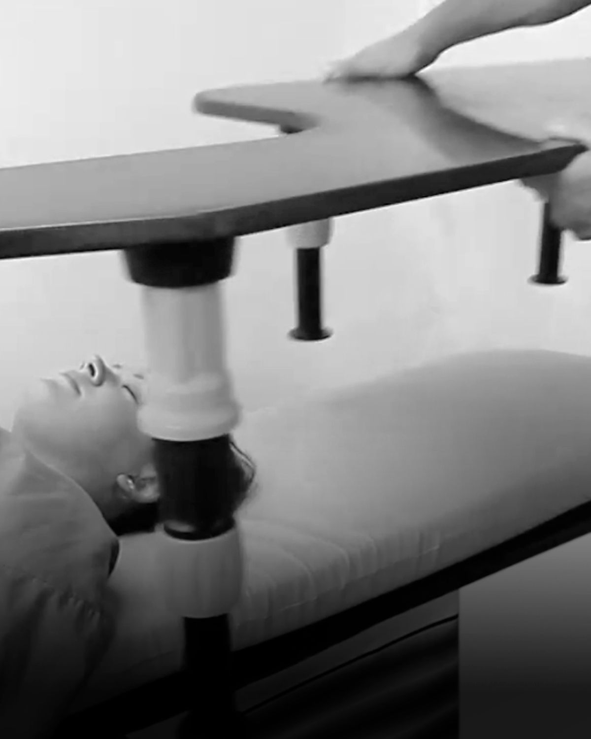 Medical professional adjusts equipment over a patient's legs on a medical table.